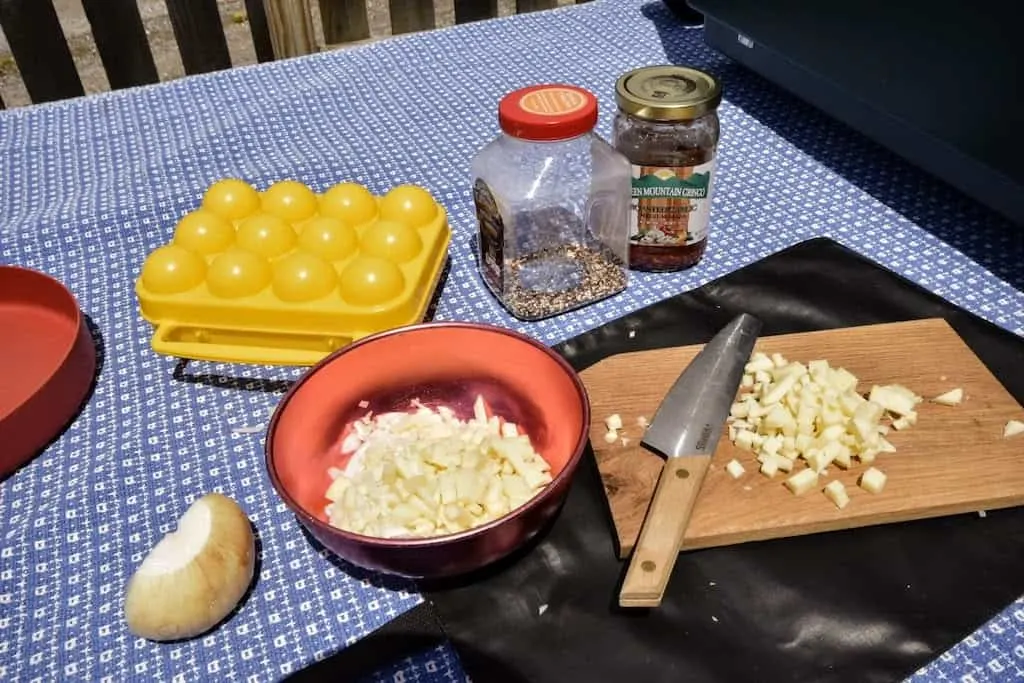 a cutting board with chopped onions and a variety of ingredients on a picnic table for camping.