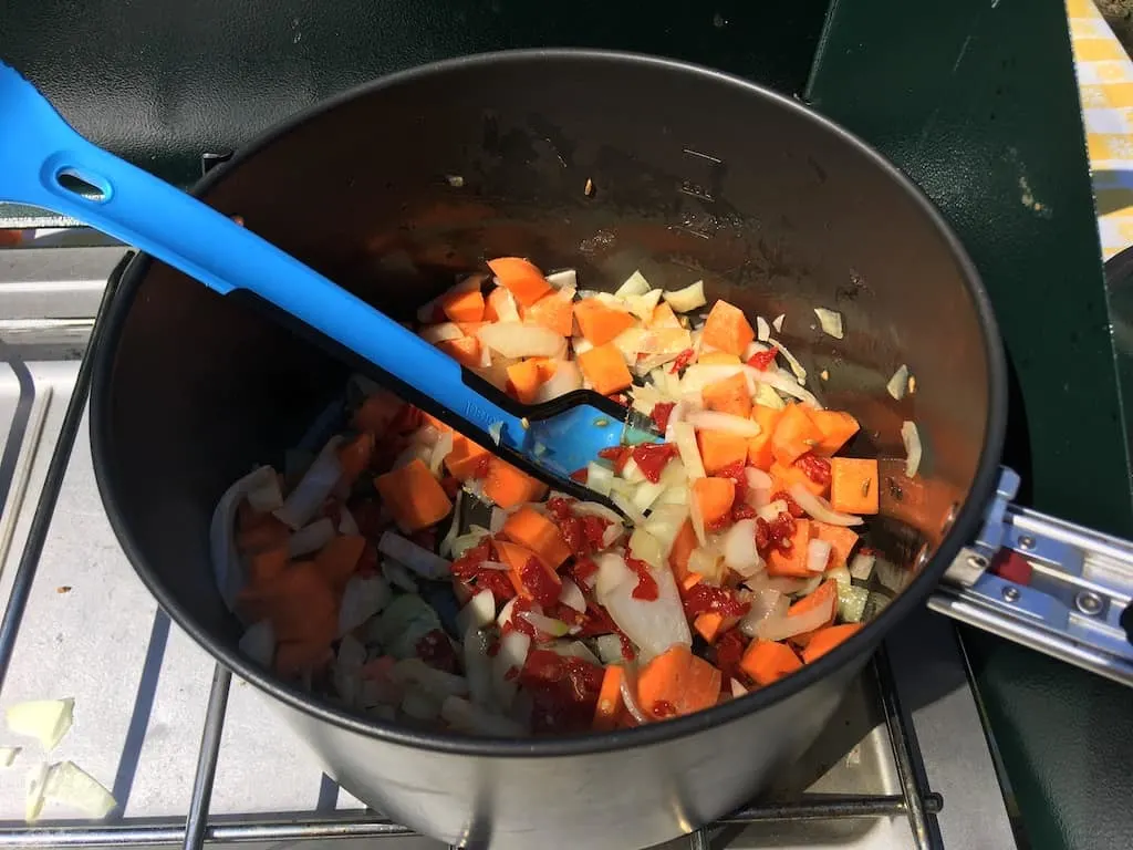 A camping pot with a bunch of chopped vegetables in it and a blue/black spork.
