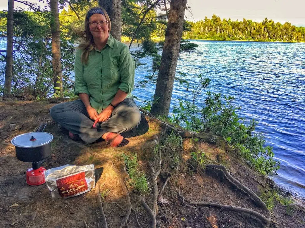 A woman cooks a backpacking meal near a beautiful mountain lake.