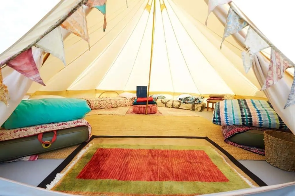 A fully decorated glamping ent with several beds, rugs, pillows, and flags inside
