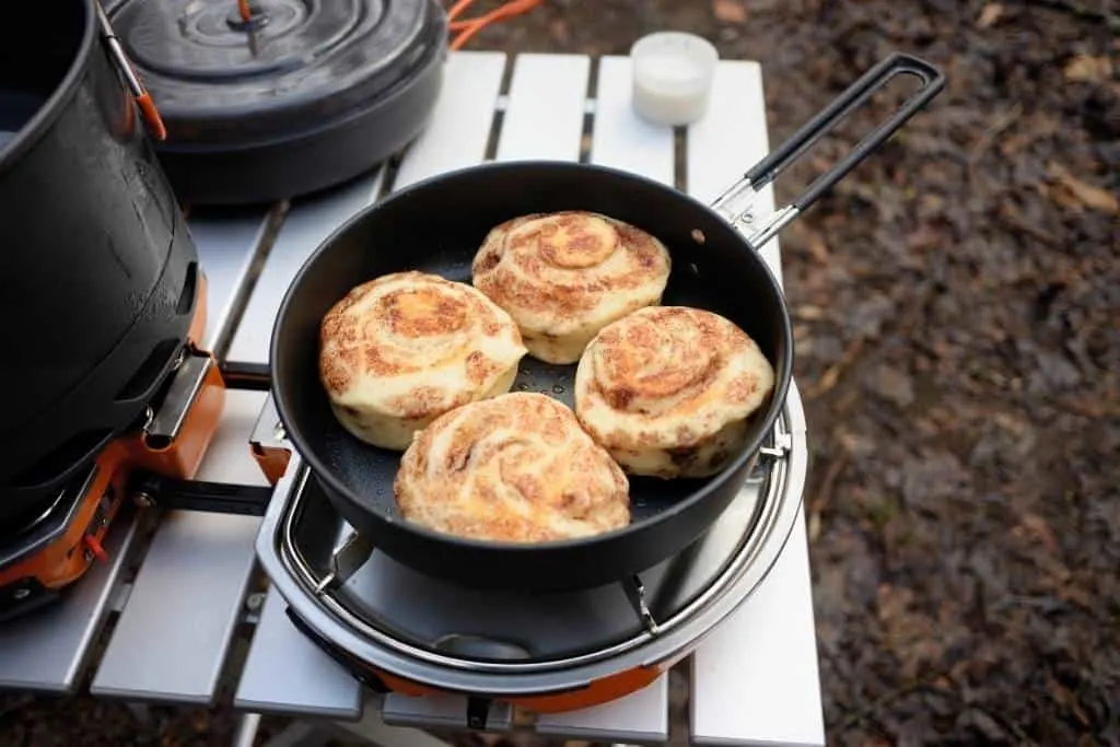 A camping table with a frying pan full of cinnamon rolls on it.