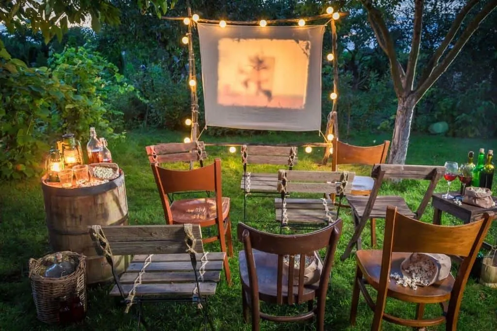 A backyard movie setup with empty chairs, candles, and twinkling lights
