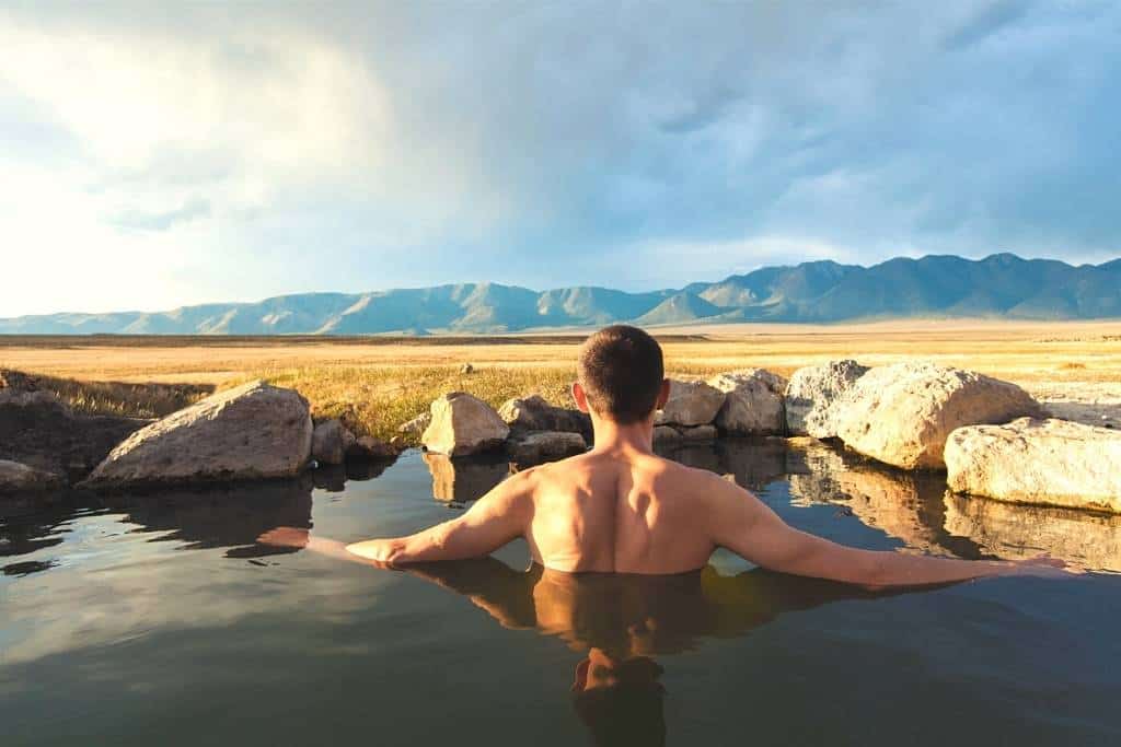 a man soaks in Wild Willy's Hot Springs in California with a stunning view of the surrounding mountain range.