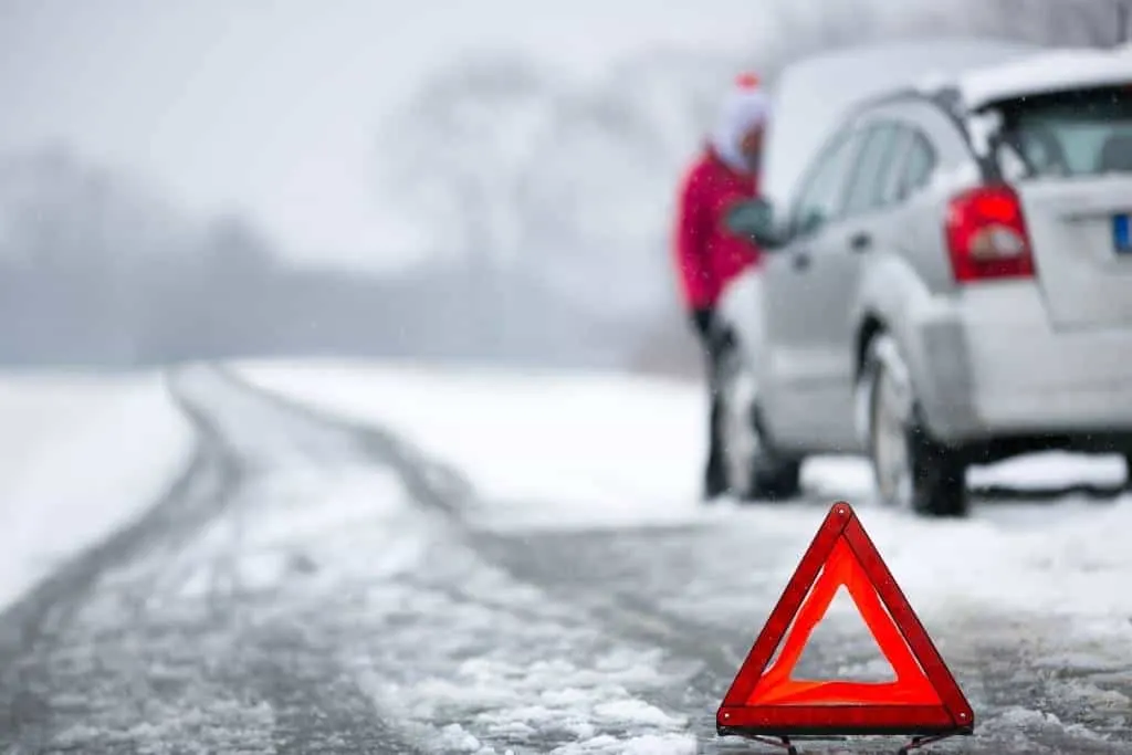 A car pulled off on the side of a snowy road with the hood open and a caution sign in front of it.