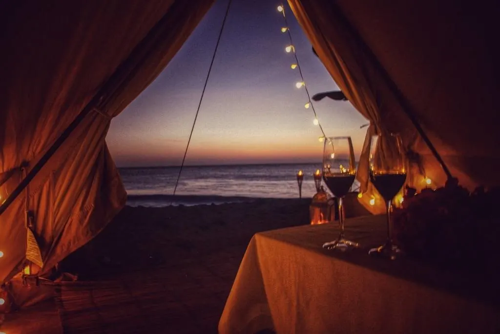 A glamping tent with two glasses of wine on a low table. You can see a view of the ocean through the tent window.