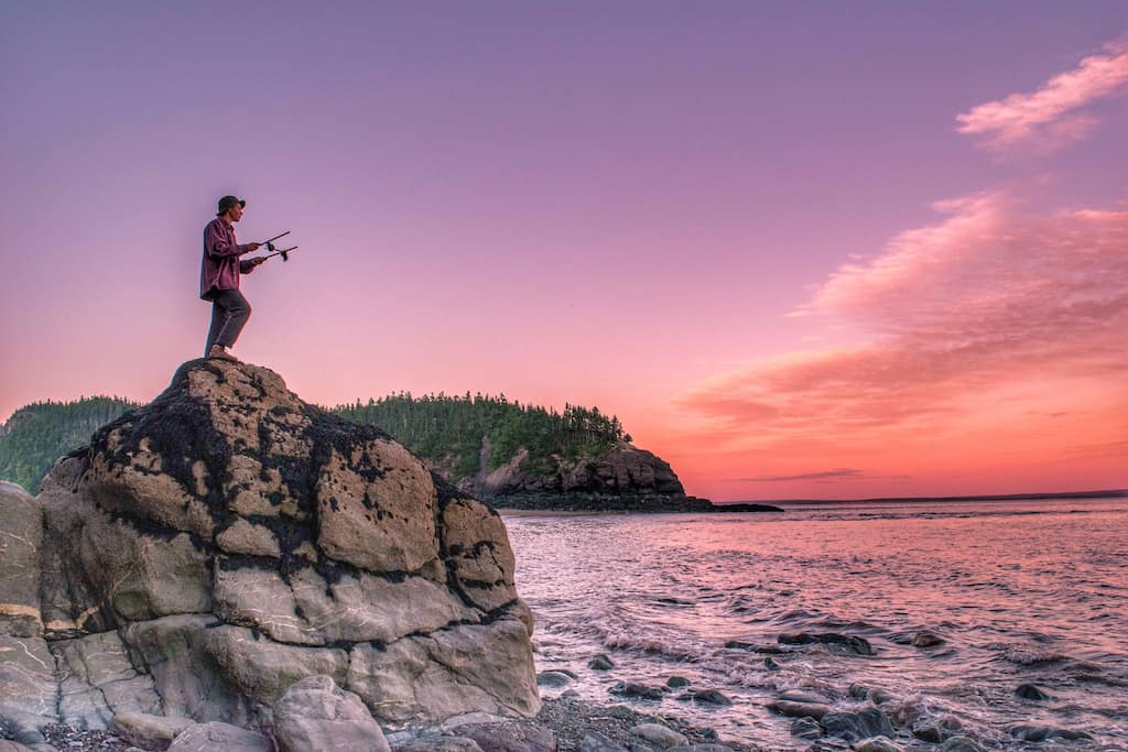 A person stands on a large rock to watch the sunset over the Bay of Fundy in New Brunswick.