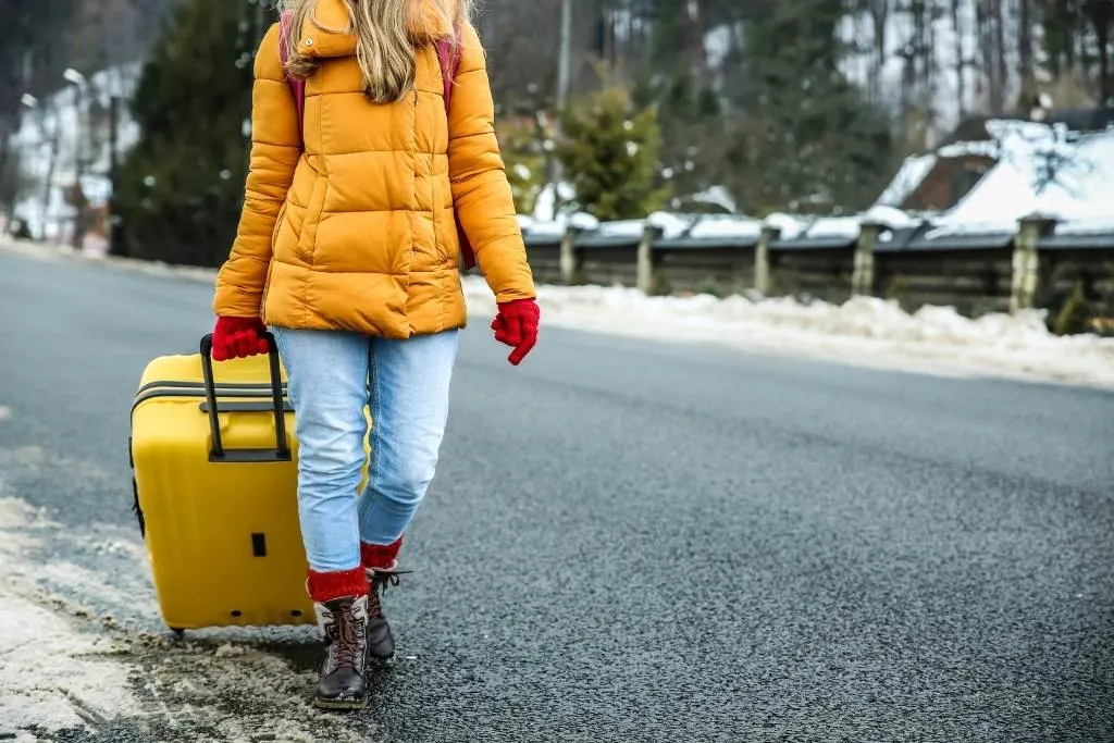 a woman in a yellow jacket pulls a yellow suitcase down the road in the winter.