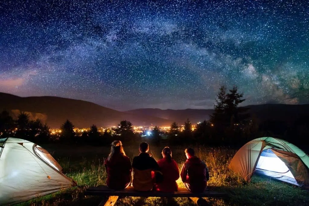 A group of friends sits around a campfire on a starry night.