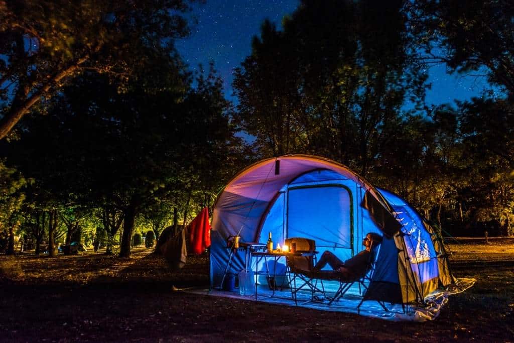 A woman relaxing near a tent in a campground at night.