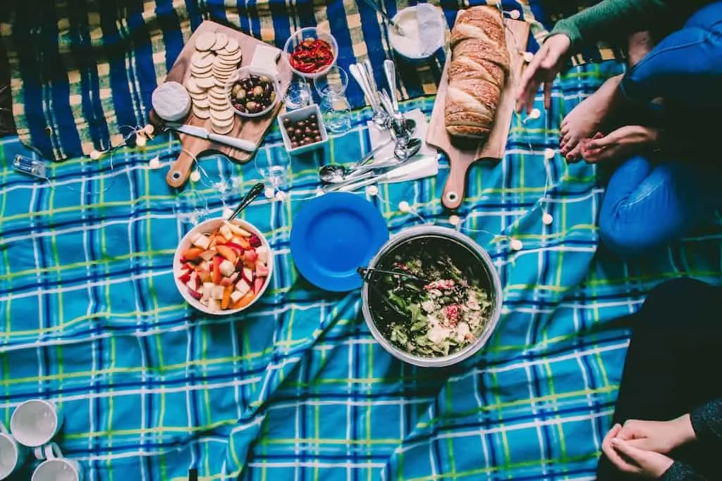 a selection of picnic food laid out on a blue checked blanket.