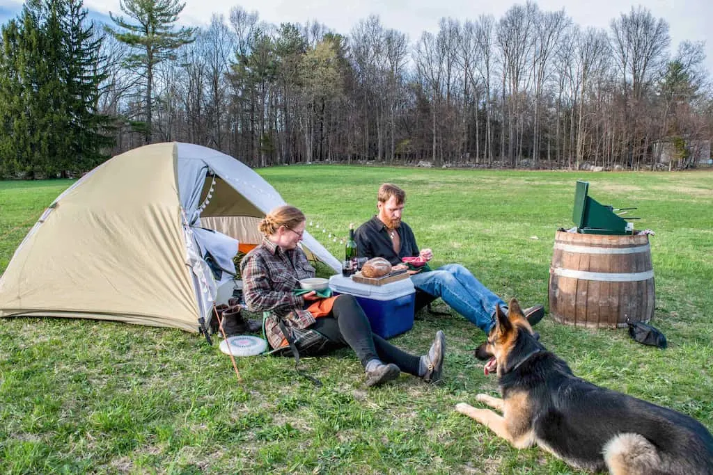 two people eat dinner in front of a small tent with a dog.