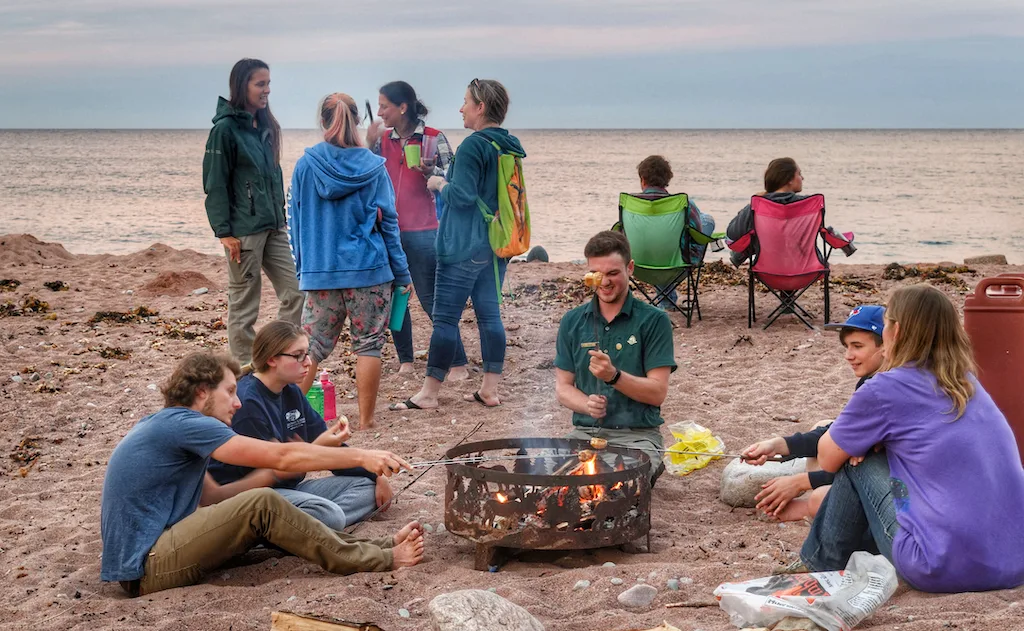 Several campers sit around a campfire on the beach at Broad Cove Campground in Cape Breton Highlands National Park.