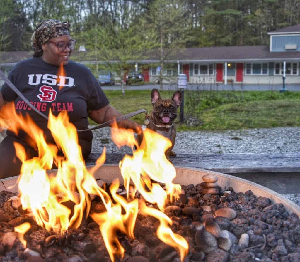 A woman sits with a French bulldog near a fire pit at the Briarcliff Motel in Great Barrington, MA.