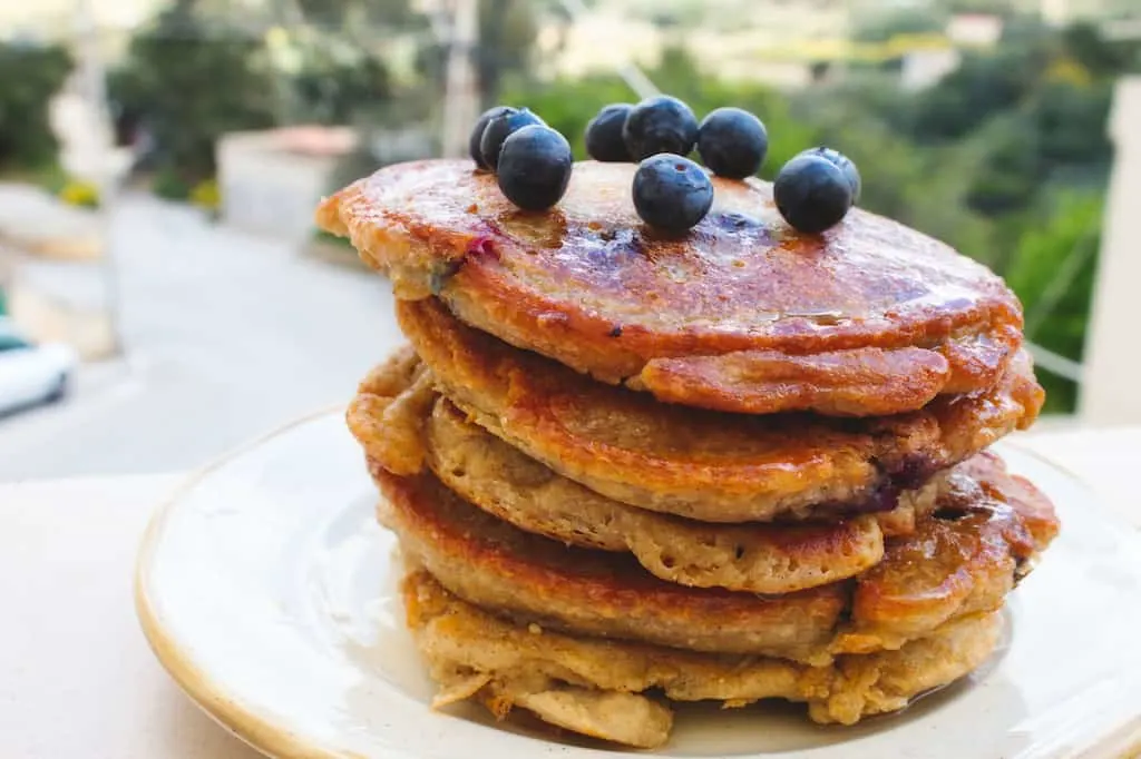 A large stack of blueberry pancakes on an outdoor picnic table.