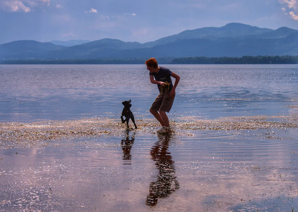 A boy plays with a small dog in Lake Champlain, Vermont.