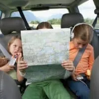 three kids in the backseat of a car looking at a map.