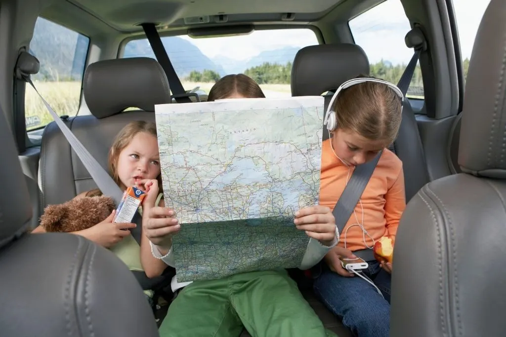 three kids in the backseat of a car looking at a map.