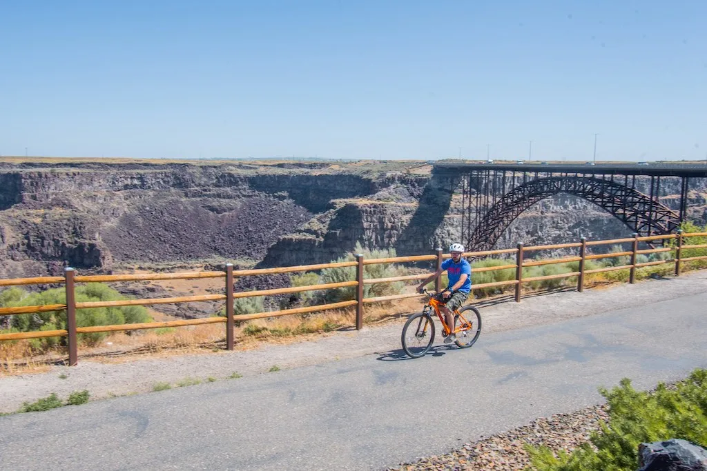 A bicyclist rides on the Canyon Rim Trail in front of the Perrine Bride in Twin Falls, Idaho. Photo credit: Visit Southern Idaho