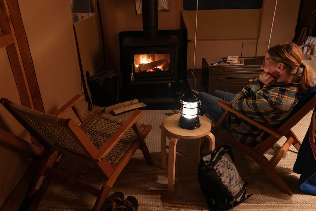 A woman sits near a woodstove while glamping in the Adirondacks at Huttopia.