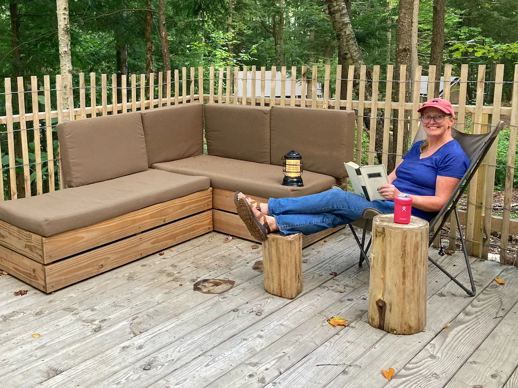 A woman sits on a balcony reading a book at Huttopia Adirondacks glamping in New York.
