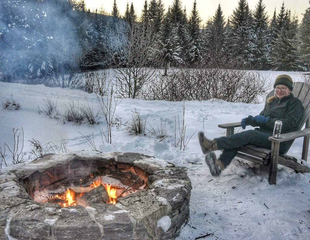 A woman sits near a winter campfire, one of the best ways to get outside more.