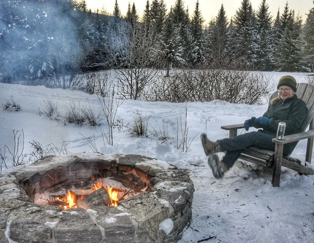 Tara sitting near a fire pit in the snow. 