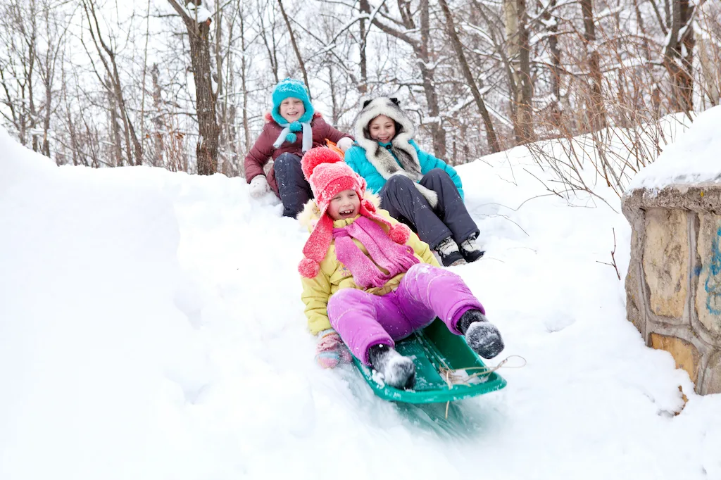 A group of three children careening down a snowy hill on plastic sleds.