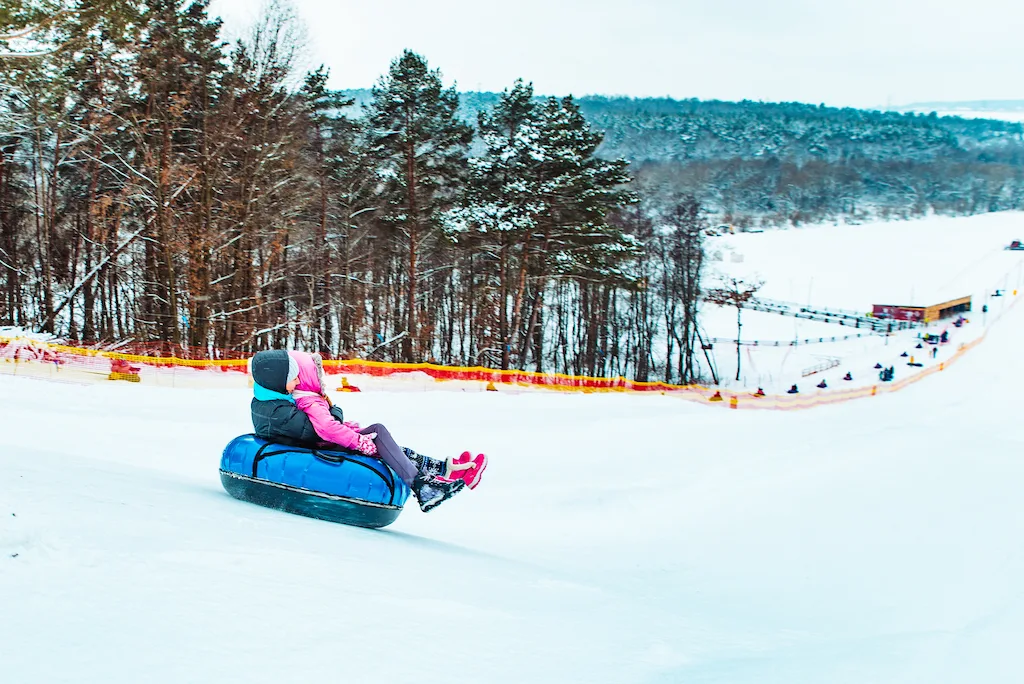 A couple sits on a snow tube as it heads down a mountain at a resort.