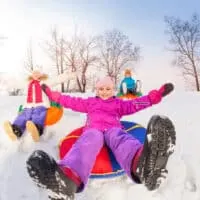 Several kids slide down a snow tubing hill on their winter vacation.