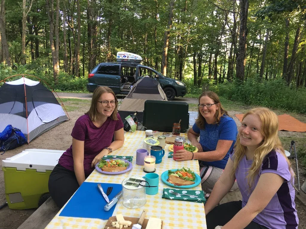 A family sits at a picnic table at a campground eating dinner.