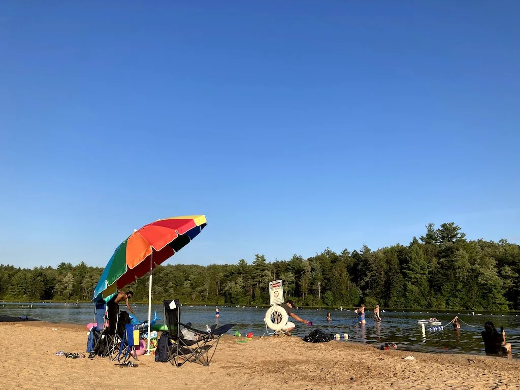 A colorful beach umbrella and people swimming at Sand Spring Lake in Hickory Run State Park in Pennsylvania.