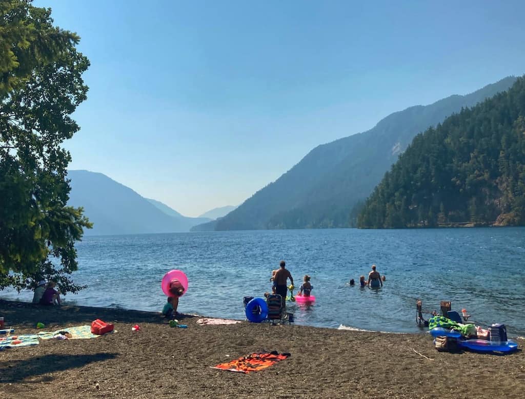 people enjoying the water from a beach on Lake Crescent in Olympic National Park.