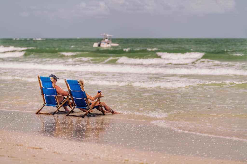 Two people sit in beach chairs on a stretch of wild beach on Caladesi Island in Florida.