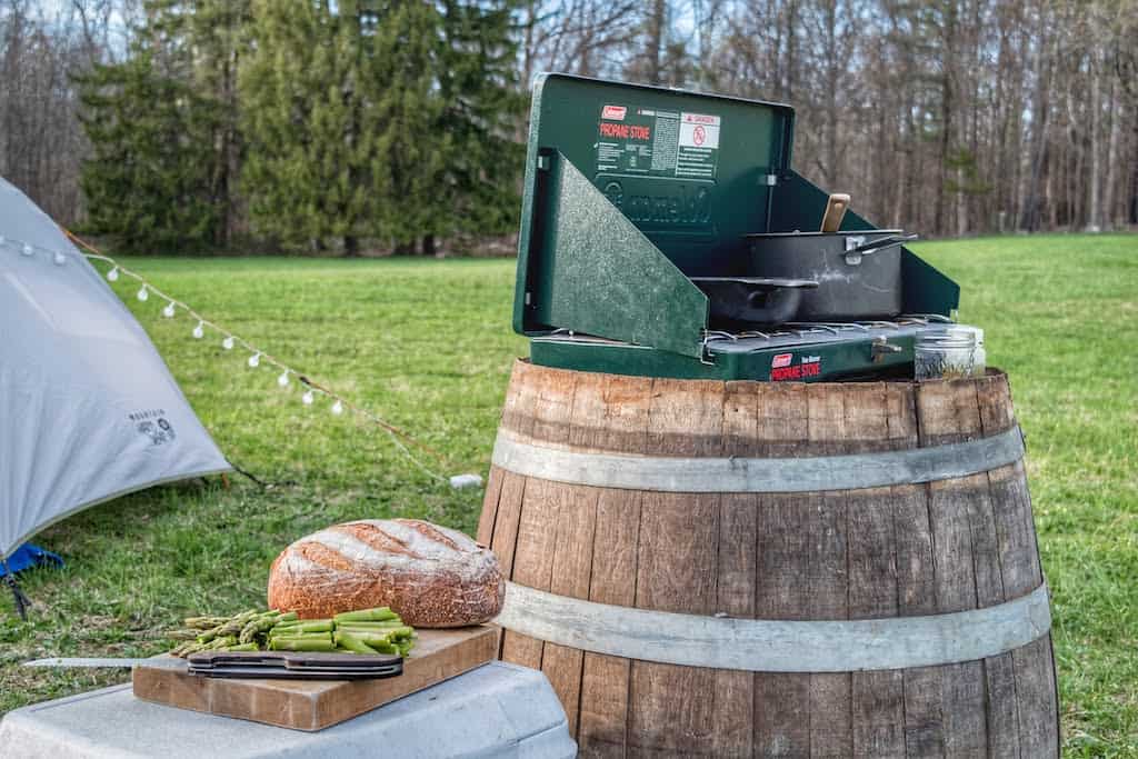 A coleman stove sits on top of a wine barrel at a campsite in New York.