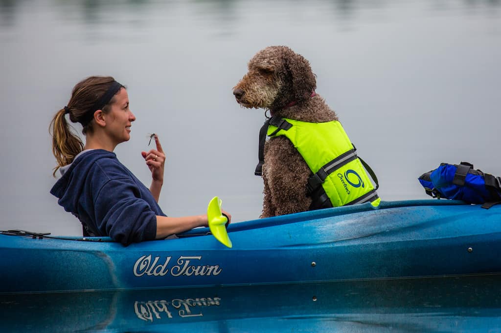A woman and a dog sit in a kayak together.