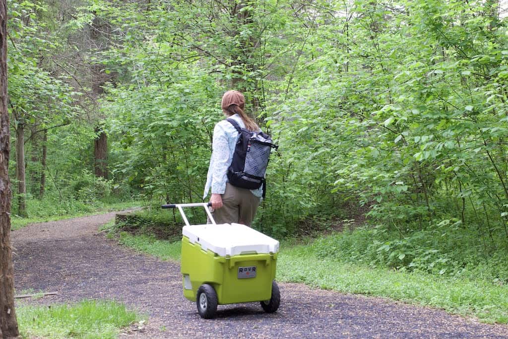 A woman pulls a wheeled cooler down a trail while camping.