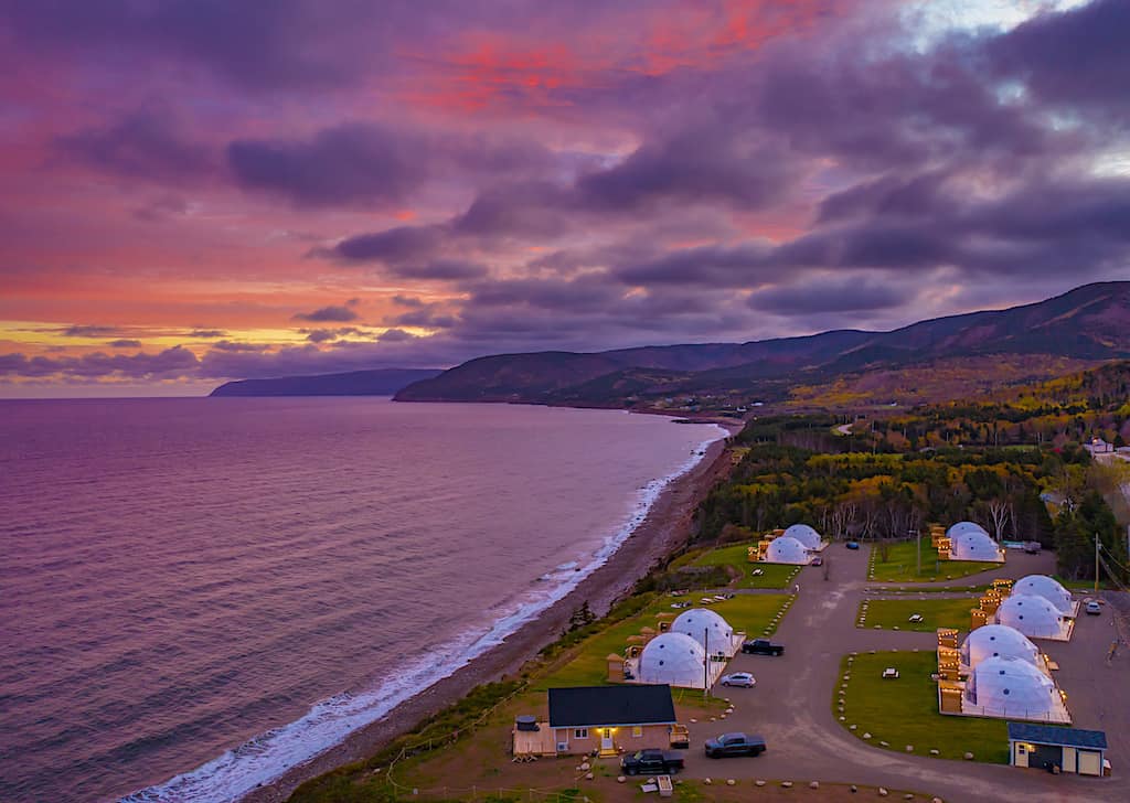 Sunset over Pleasant Bay in Cape Breton as well as several domes that are part of a glamping resort.