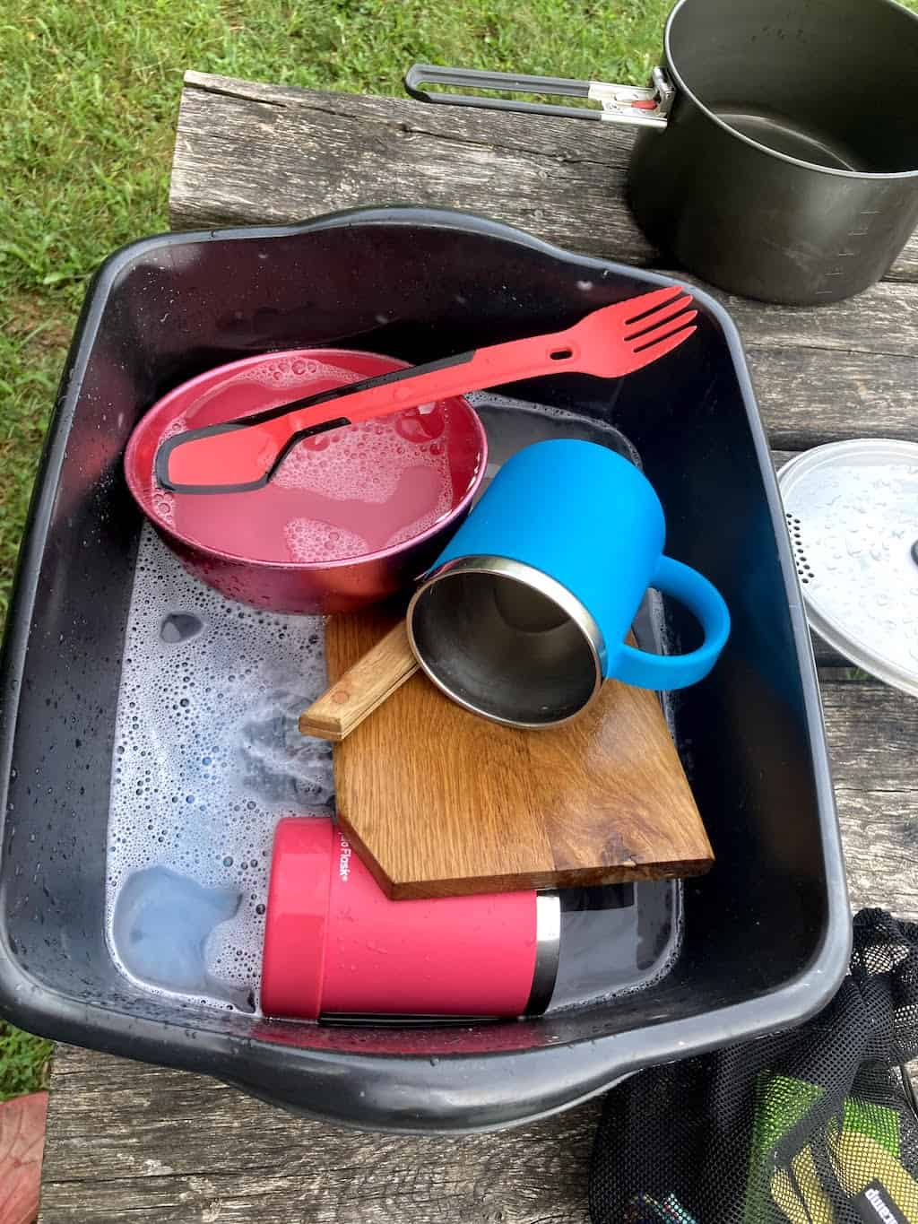 A plastic tub full of camping dishes for washing.