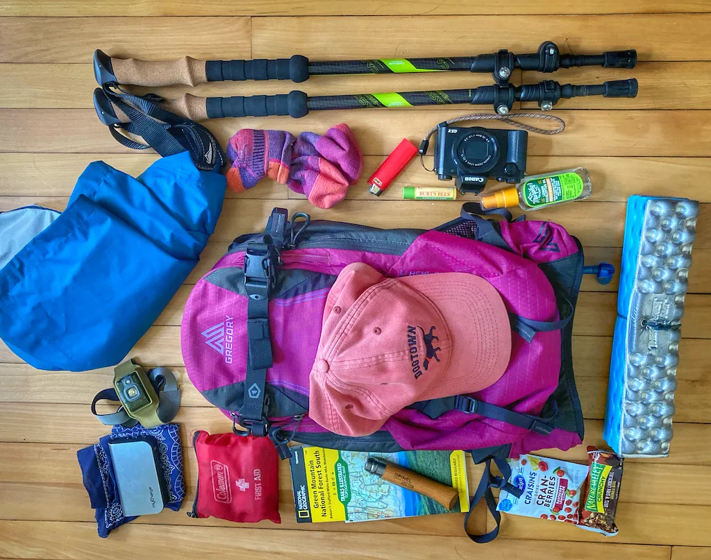 A flat-lay photo of day hiking essentials surrounding a purple day pack. 