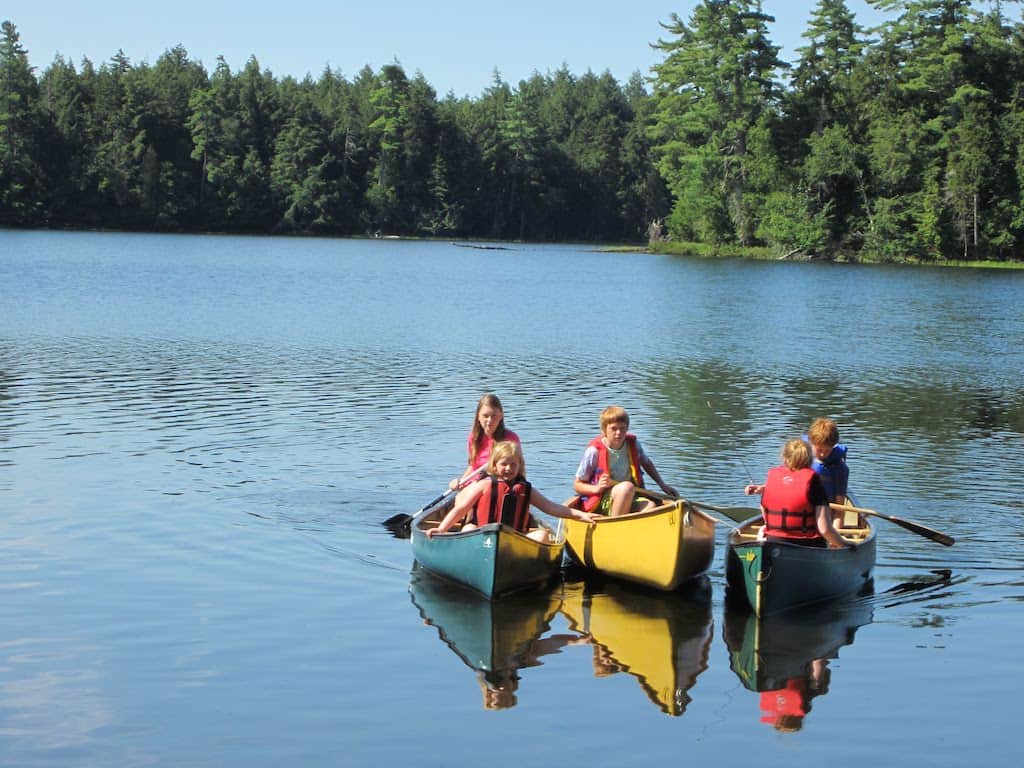 Three side-by-side canoes with kids in them in New York's Adirondack Park. 