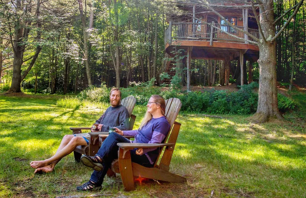 Tara and Eric sitting in Adirondack chairs in front of a treehouse.