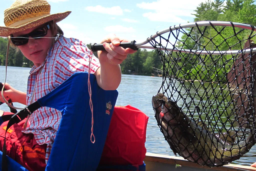 A boy holds a net with a large fish in it.