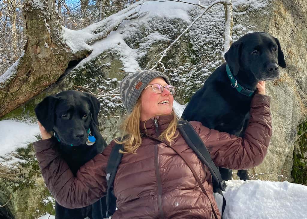 Tara wearing a warm puffy coat with her two labs on a winter hike. 