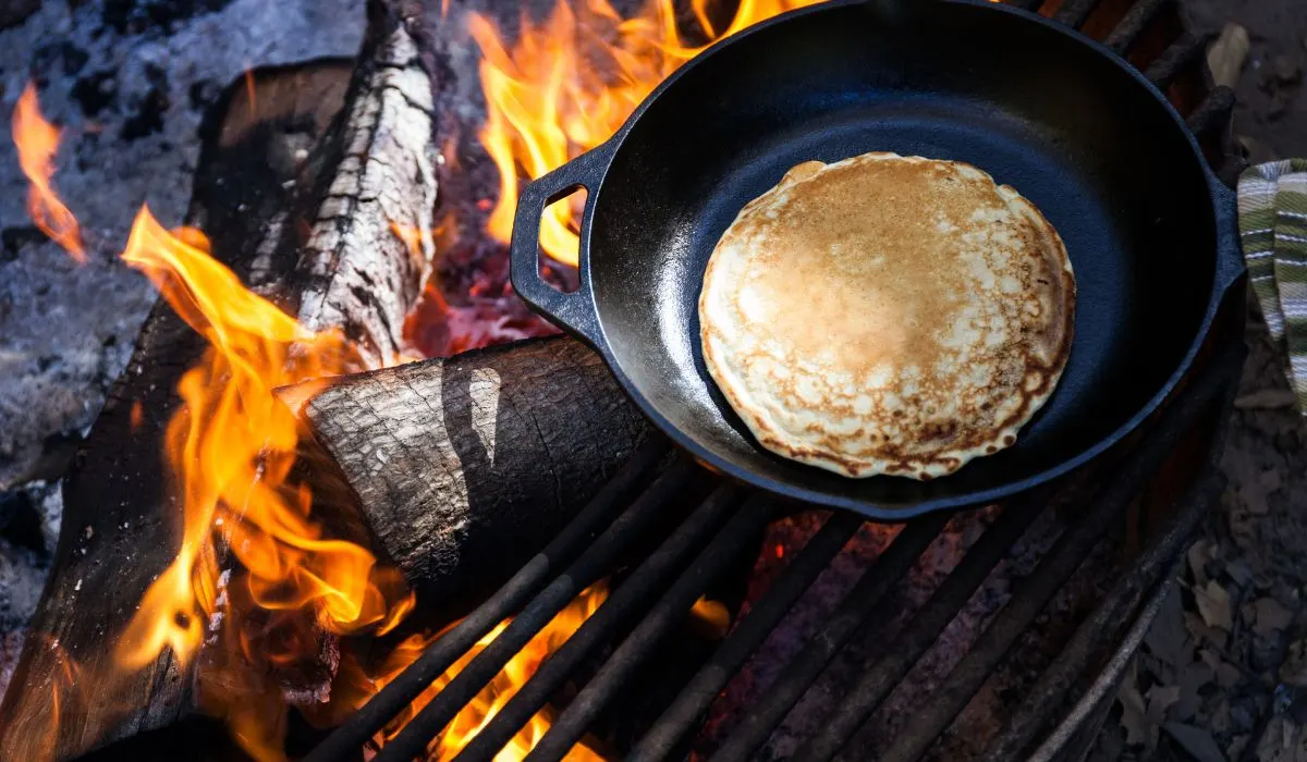 A cast iron skillet with a pancaked over an open fire. 