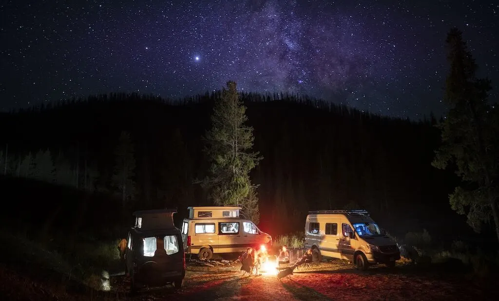 Campervans around a fire with a starry sky. 