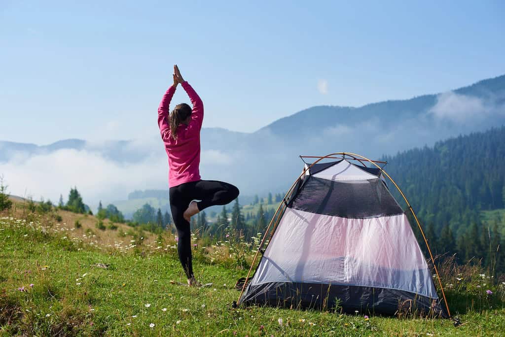 A woman doing yoga next to a tent in the spring.