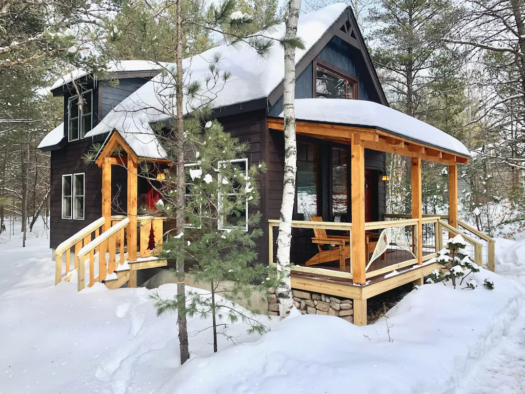 Tiny grey cabin in New York covered with snow.