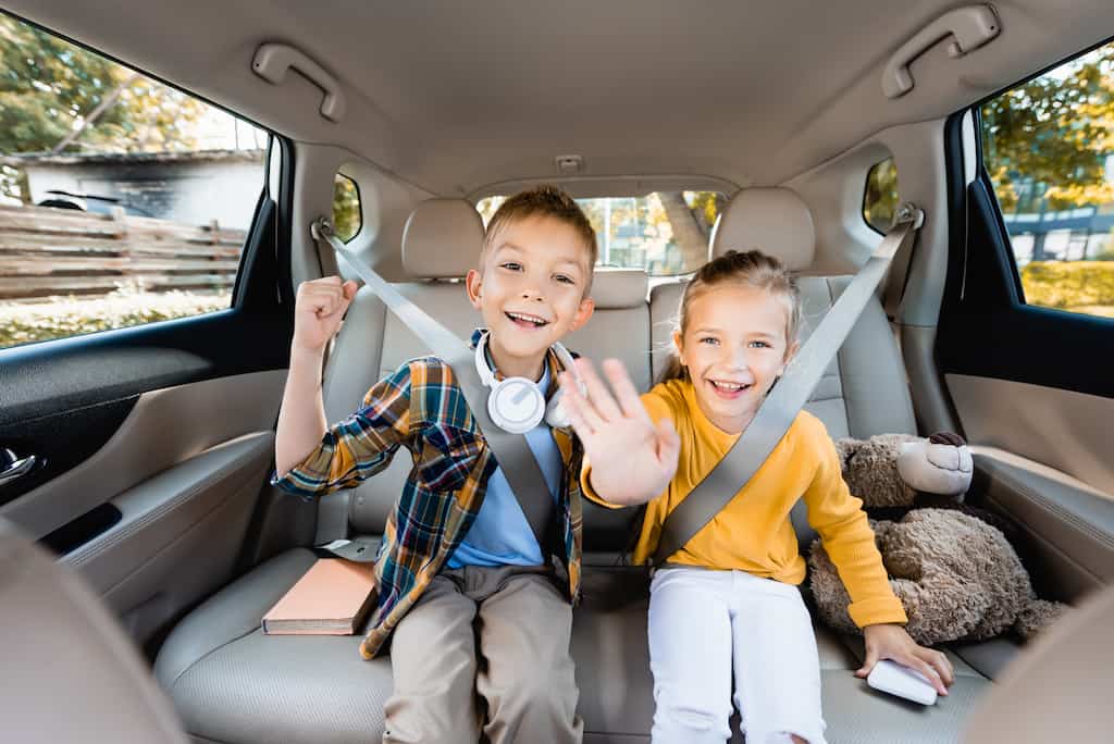 Two kids happily sitting in the backseat of a car.