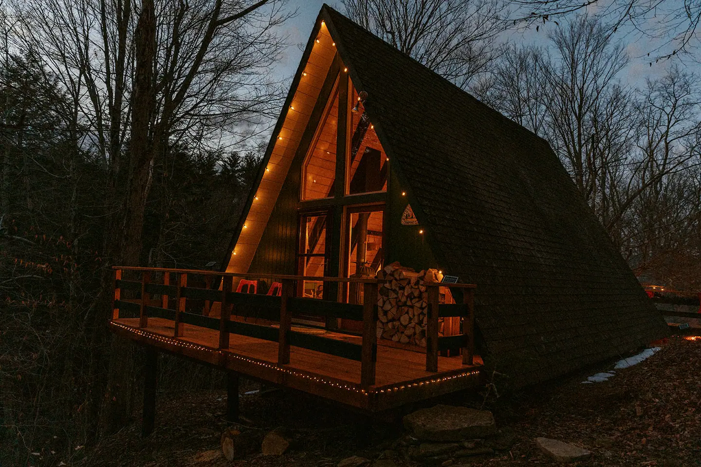 An A-frame vacation rental with twinkly lights and a huge stack of firewood on the porch.