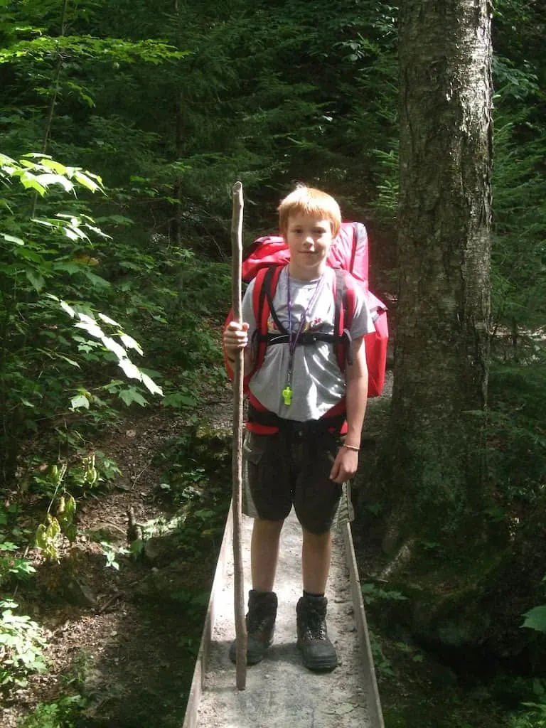 Rowan standing on a footbridge in the woods wearing a backpack.